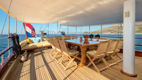 Spacious outdoor deck of the gulet Linda with a large dining table and a Croatian flag in the background.